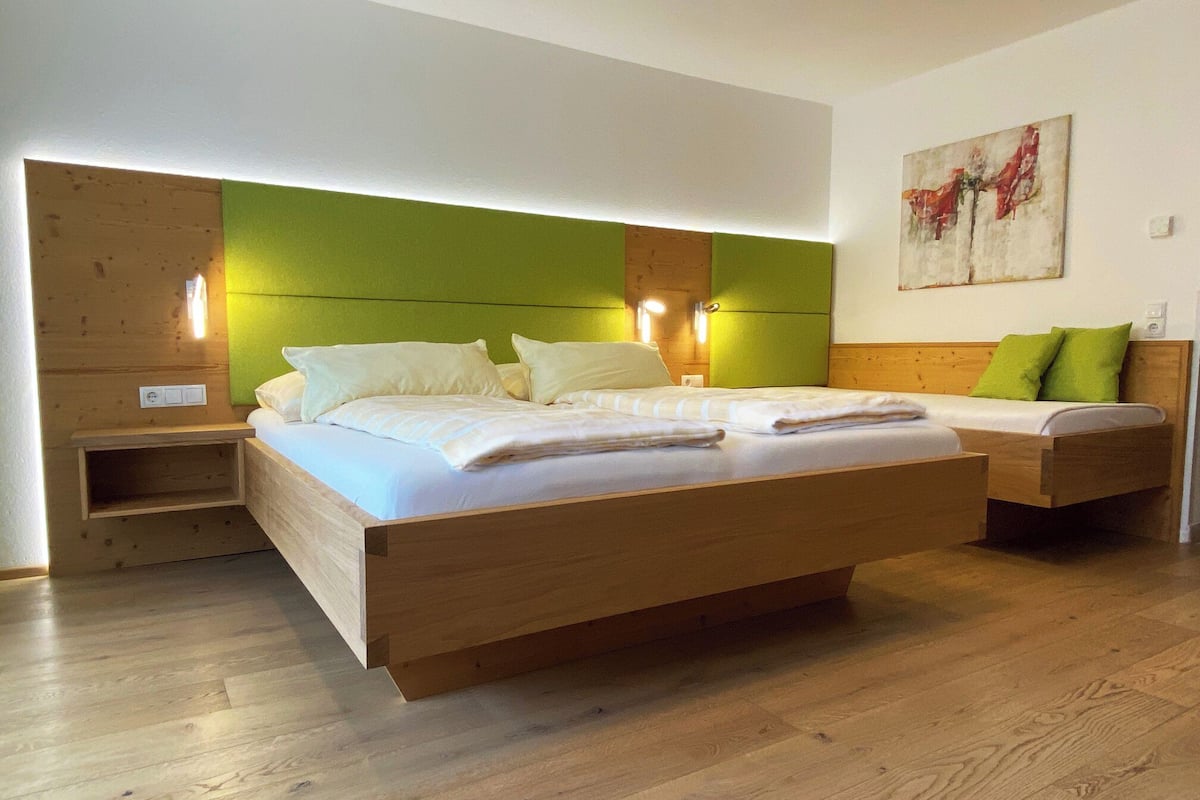 Quarto moderno com cama de madeira, mesas de cabeceira e uma parede verde de destaque.