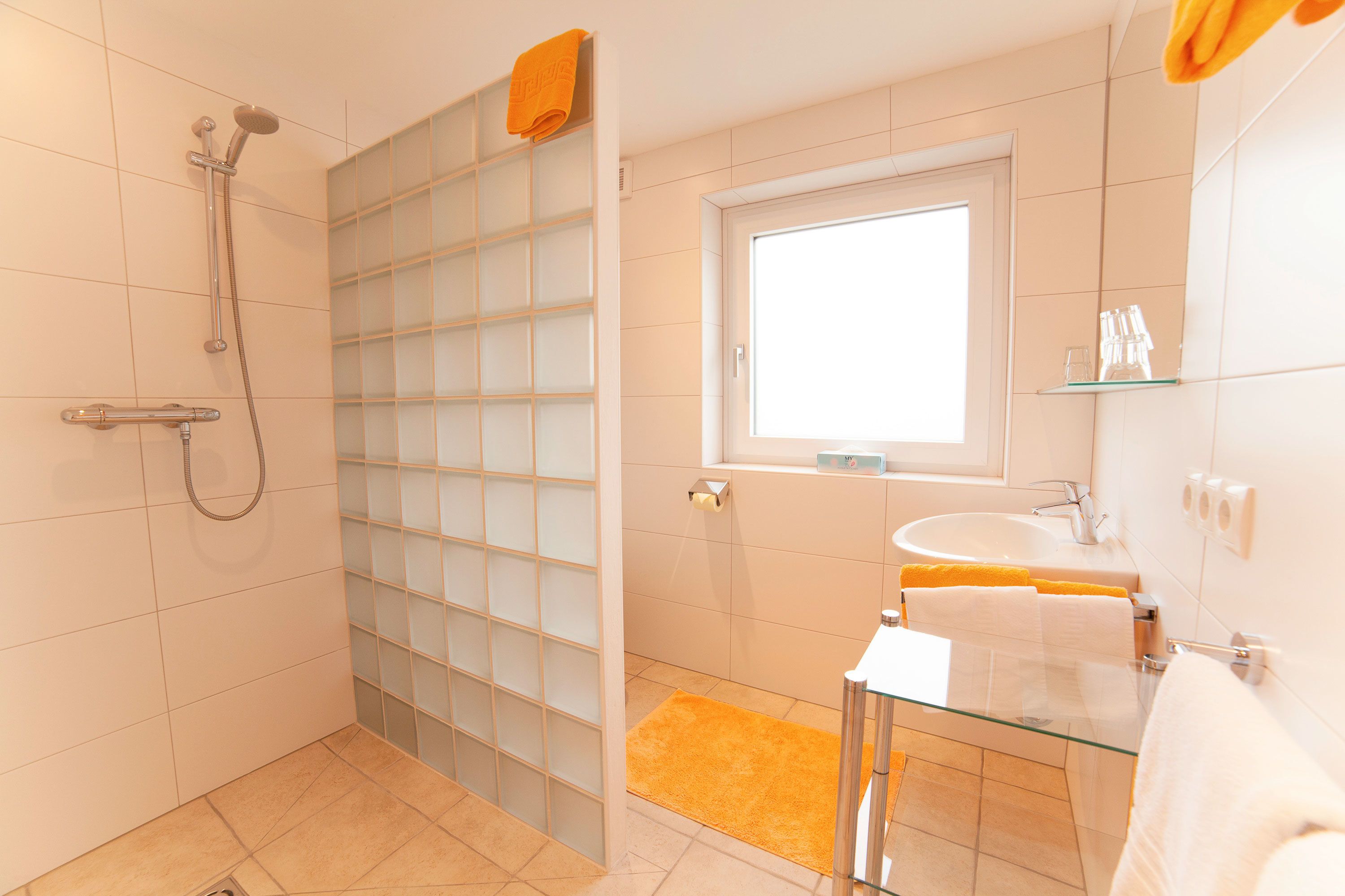 A bathroom with a glass shower enclosure, a window, a sink, and a mirror.