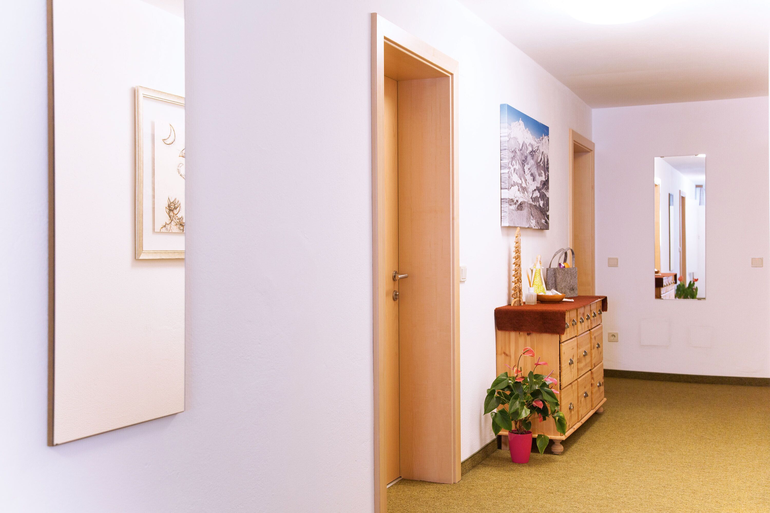 A hallway with a wooden door, a dresser with a mirror, and framed artwork on the walls.