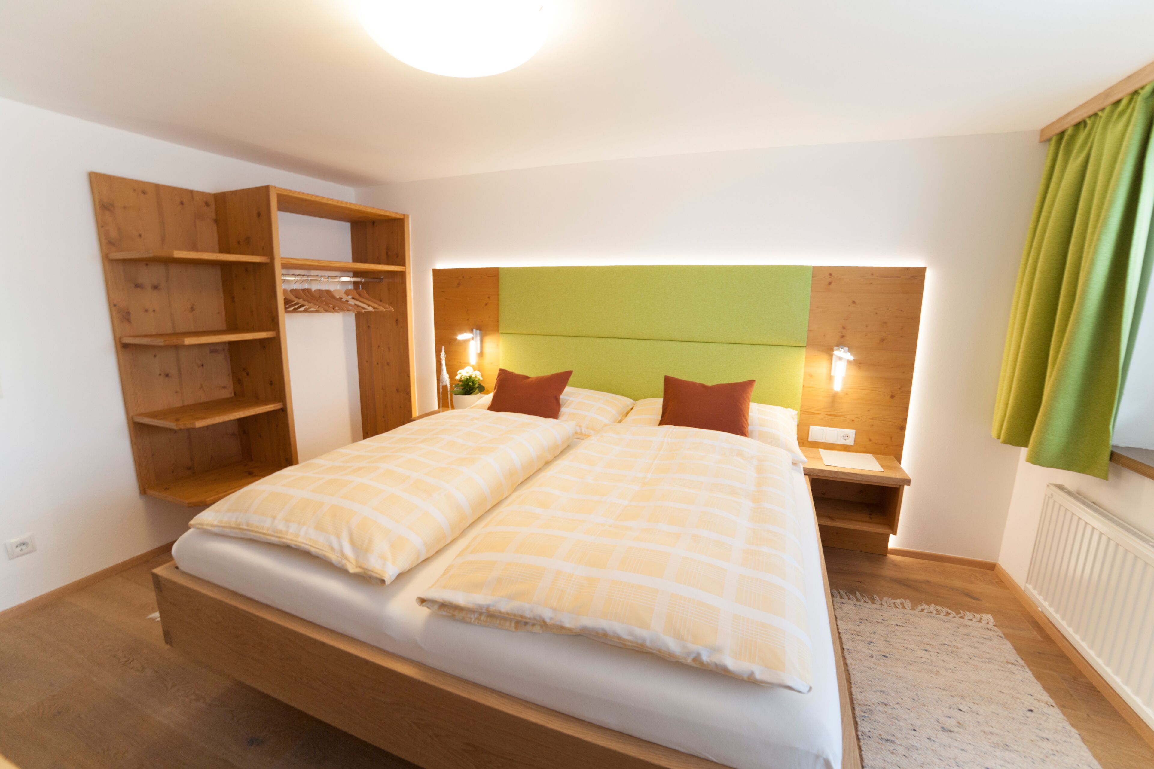 A bedroom with a wooden bed, a built-in wardrobe, bedside tables with lamps, and a green headboard.