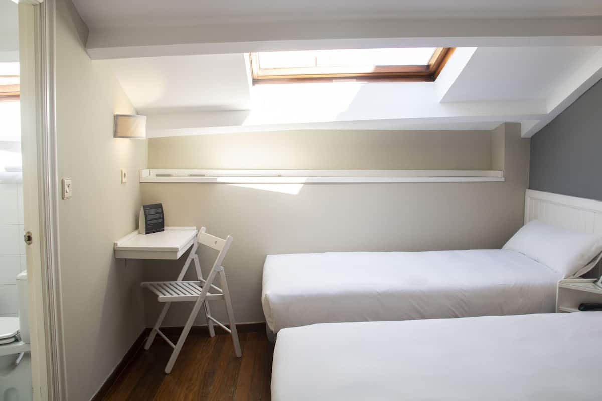Un dormitorio con dos camas, un escritorio, una silla y un tragaluz.