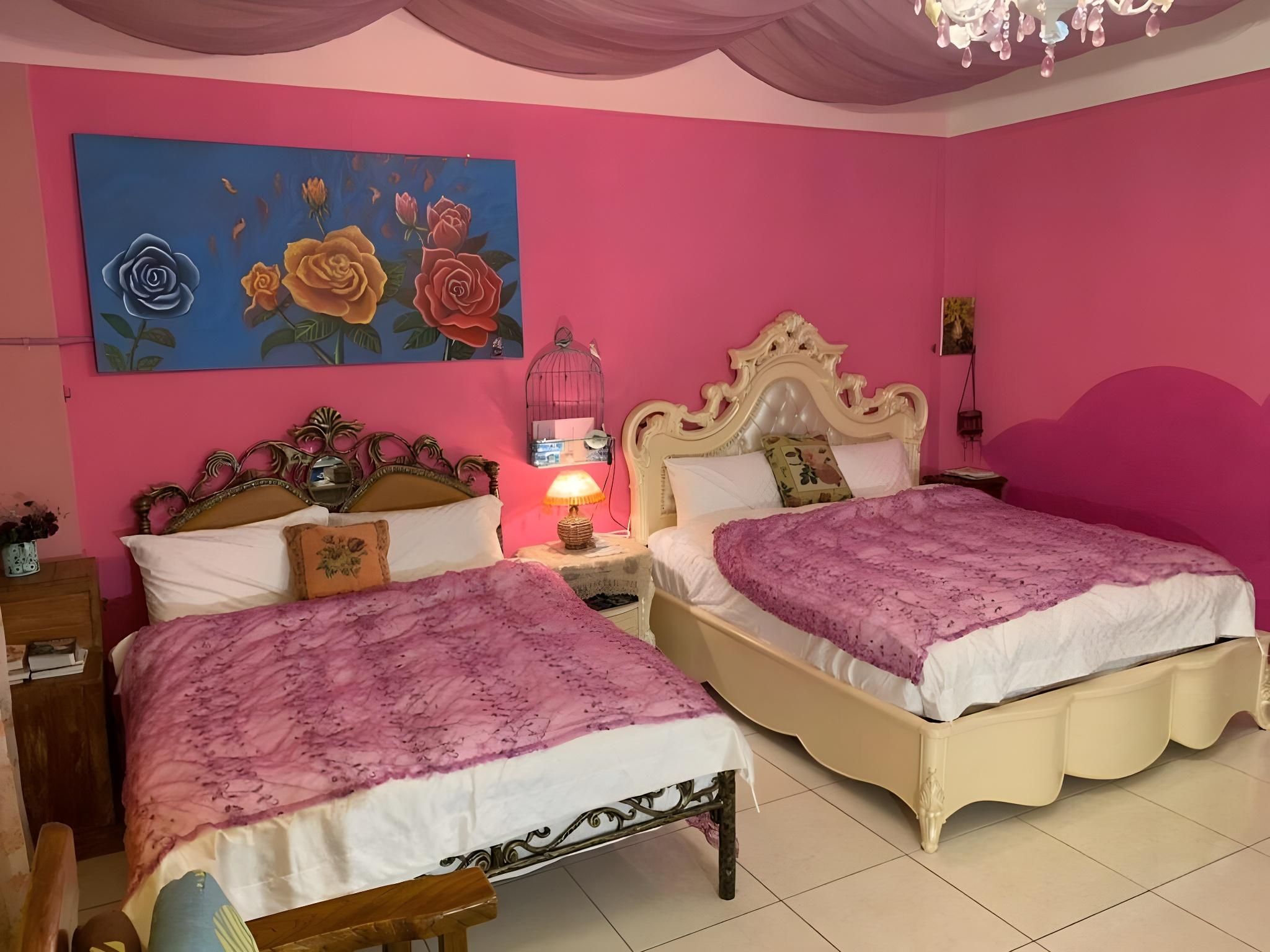 A bedroom with two beds, a pink wall, and a painting of roses.