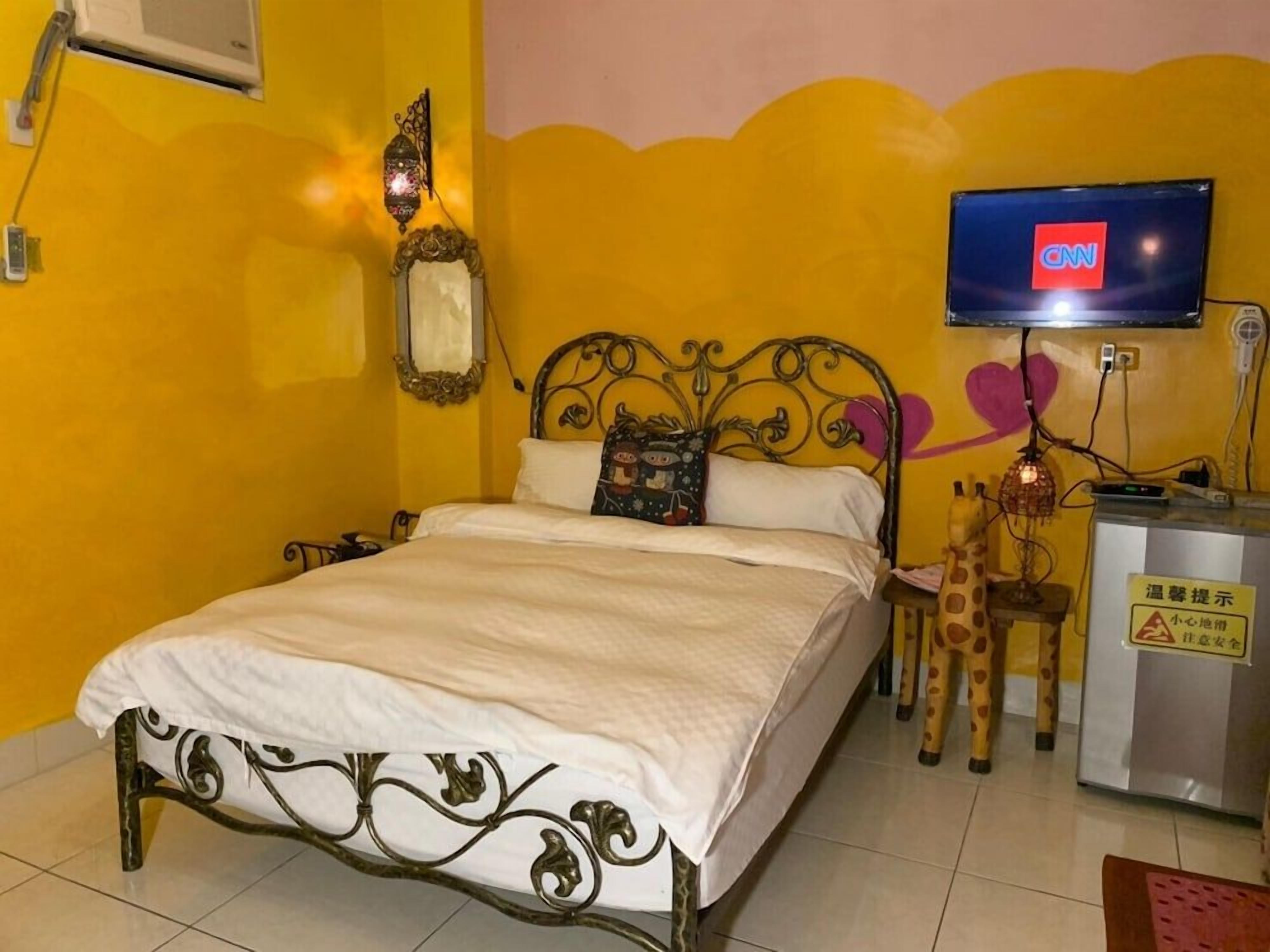 A bed with a decorative headboard, a television on a stand, a small table with a giraffe figurine, and a wall-mounted lamp.