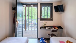 Habitación de hotel con dos camas, un escritorio con silla, un televisor montado en la pared y una ventana con vistas al exterior.