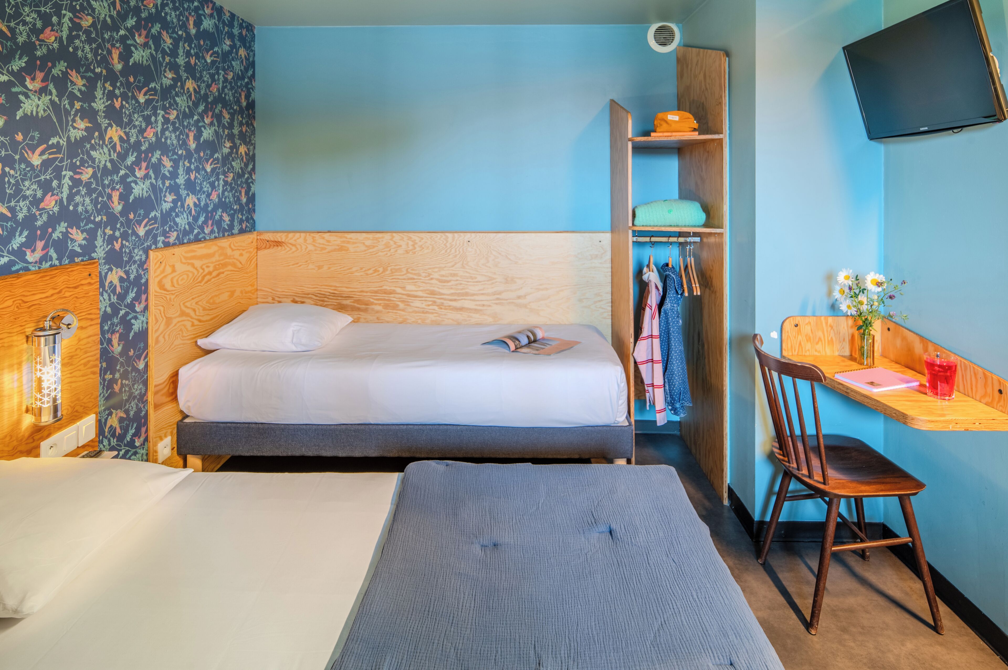 A bedroom with a bed, a desk with a chair, a wardrobe, and a television.
