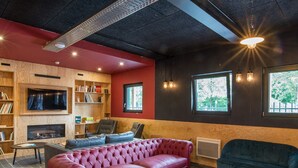 Una sala de estar moderna con un sofá de cuero rojo, un sillón azul y una mesa de centro blanca. Hay una chimenea, estanterías y un ventanal que ofrece vistas al exterior.