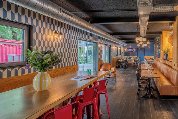 A restaurant interior with a long wooden bar, red chairs, and a patterned wall. - Eklo Hotels Lille (Lille)