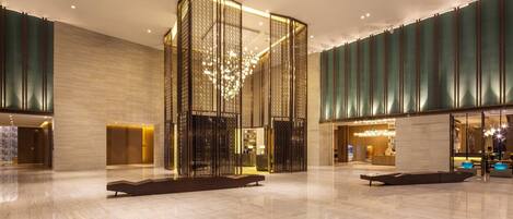 A spacious lobby with a modern design, featuring a central decorative structure, seating areas, and a reception desk.