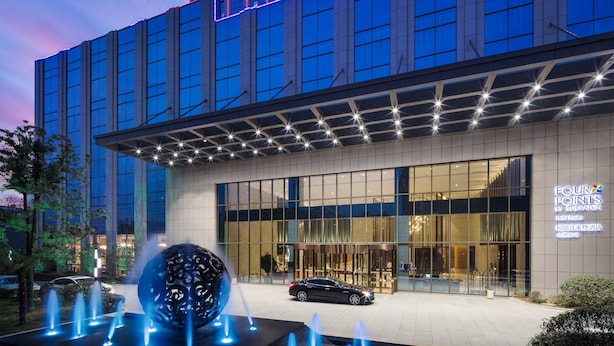 A modern hotel with a glass facade, a large spherical sculpture in the foreground, and a car parked in front. - Four Points by Sheraton Hefei, Baohe (Hefei)