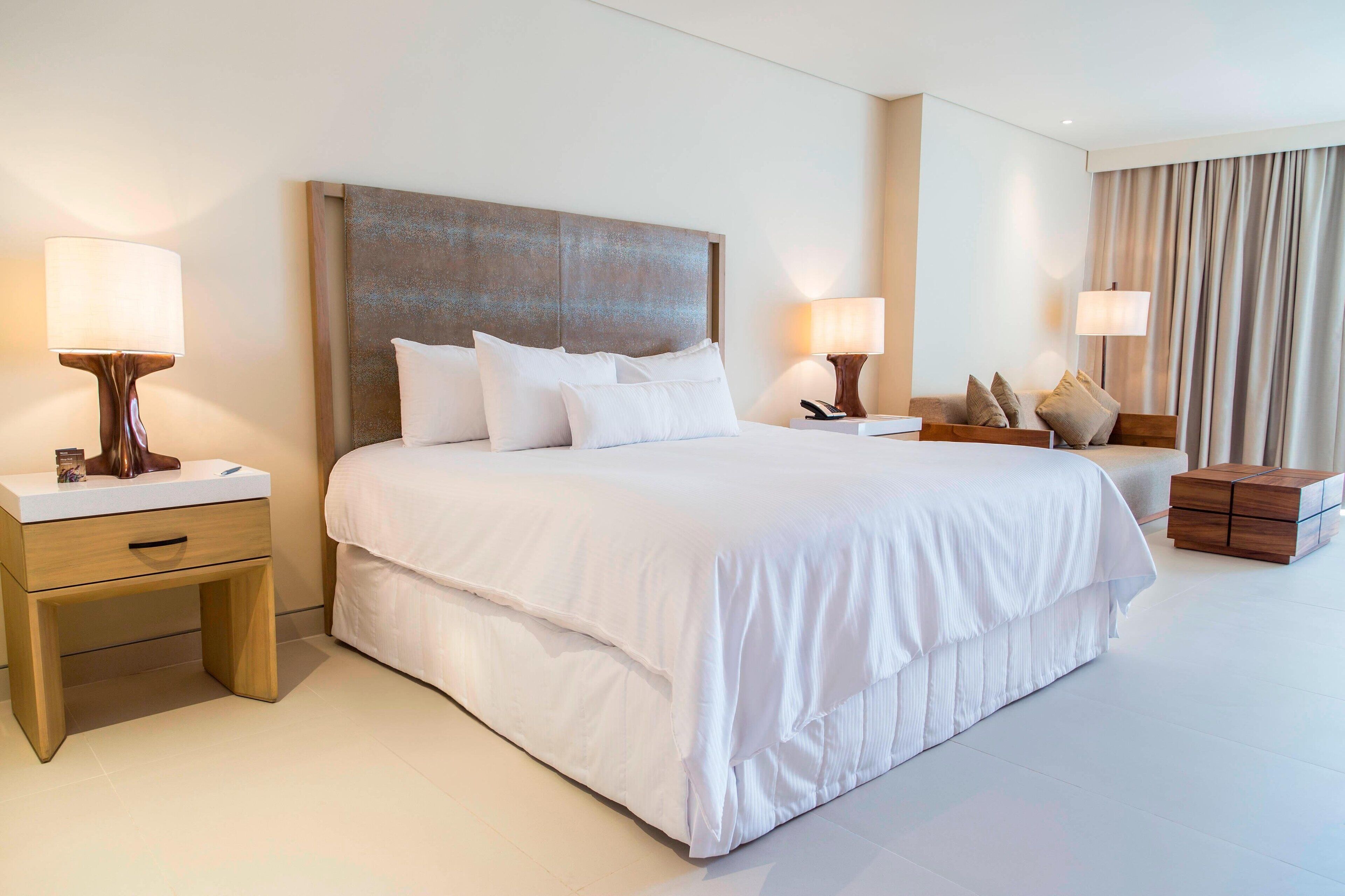 Habitación de hotel con una cama grande, dos mesitas de noche y una mesita auxiliar de madera.