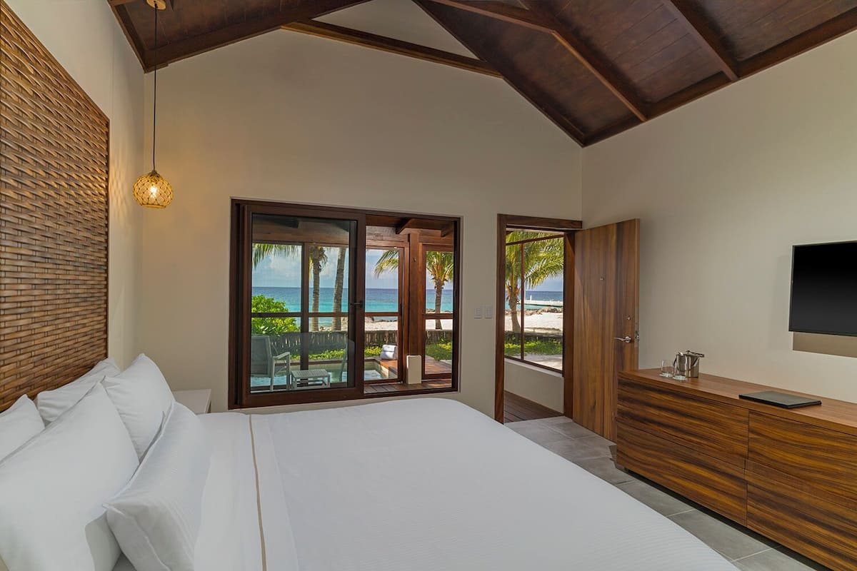 Un dormitorio con una cama grande, un aparador de madera, un televisor y vistas a la playa.