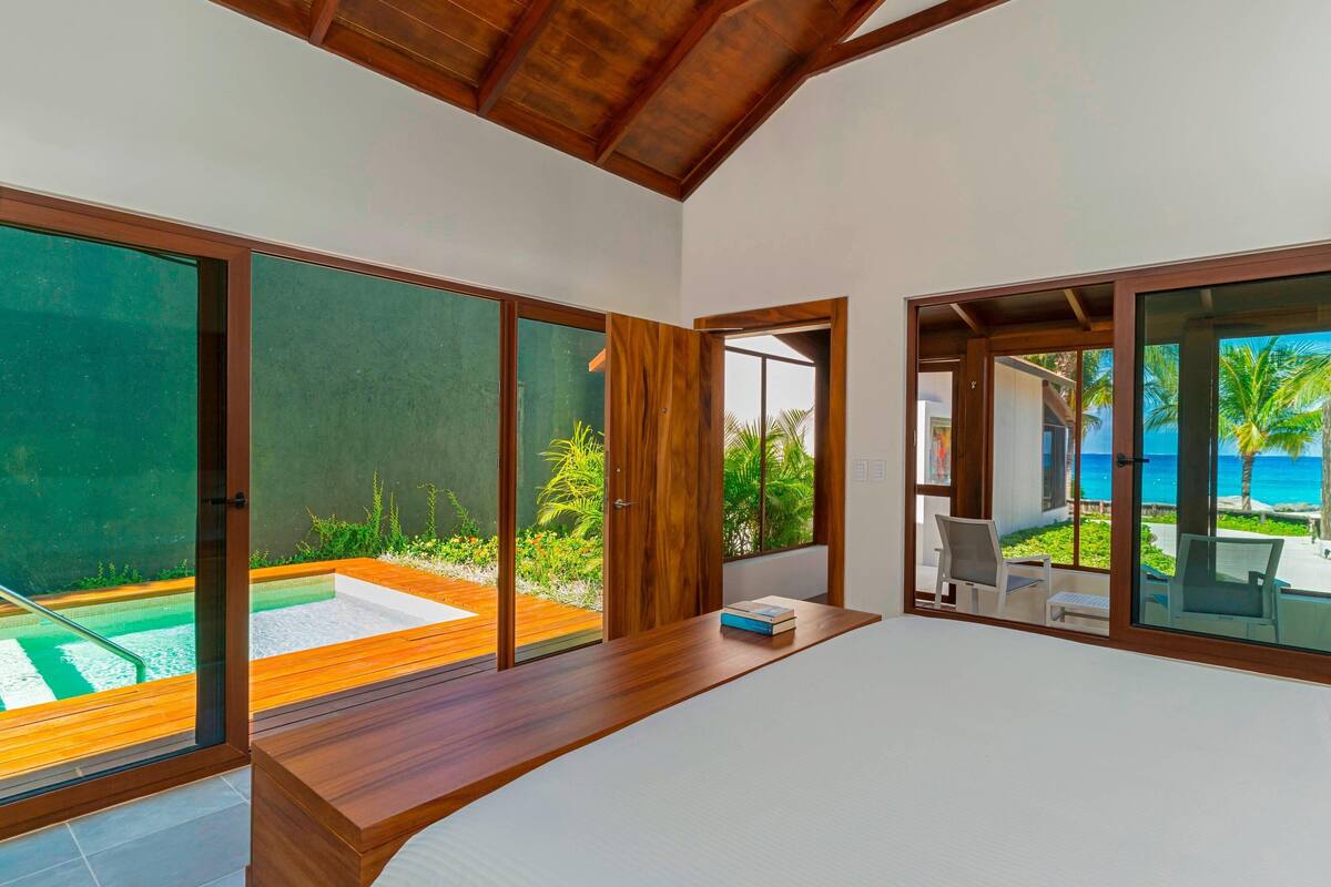 Una habitación moderna con un escritorio de madera, vistas a una piscina y una puerta de cristal que da a un área exterior con sillas.