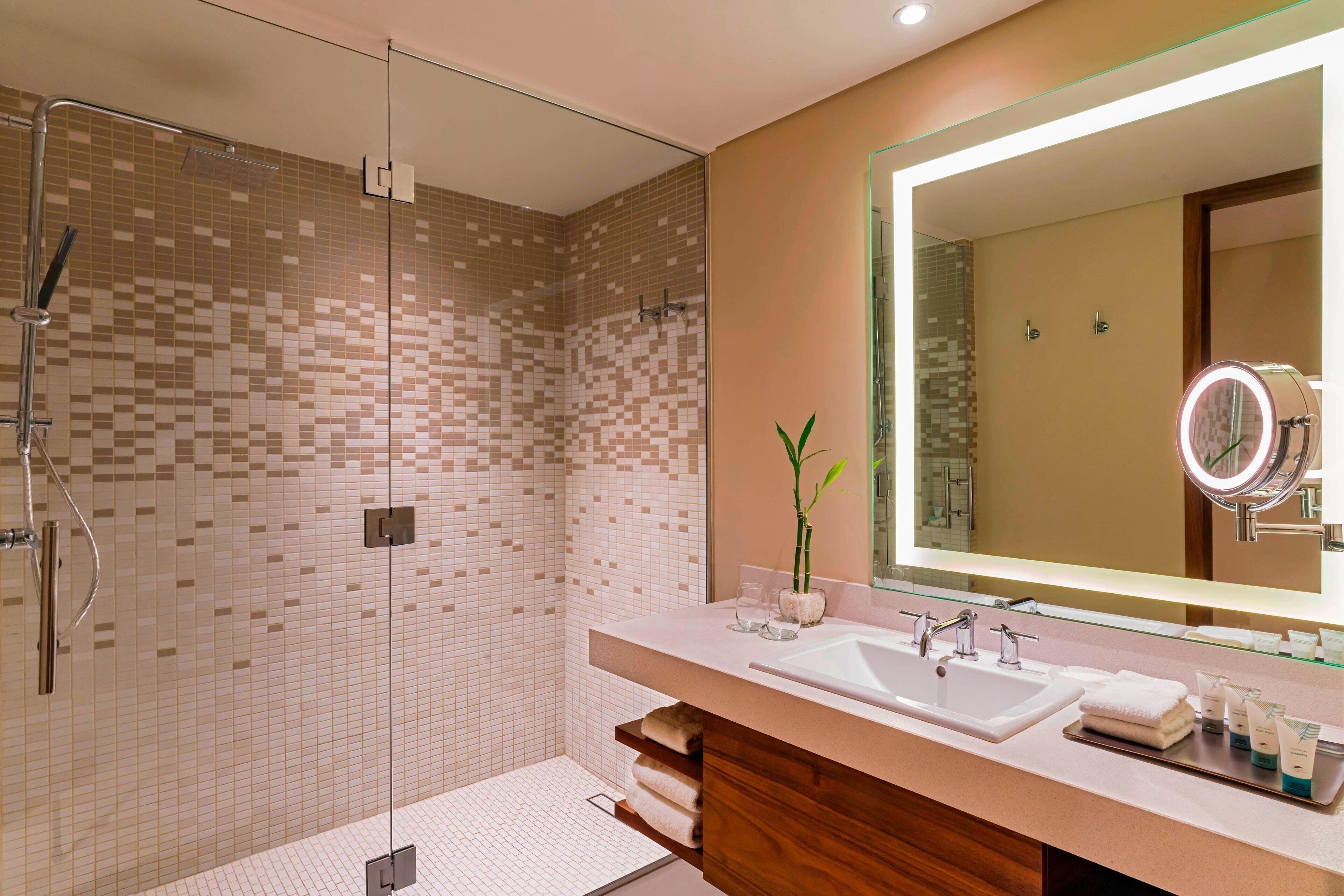 A modern bathroom with a glass-enclosed shower, a large mirror, and a vanity with a sink and toiletries.