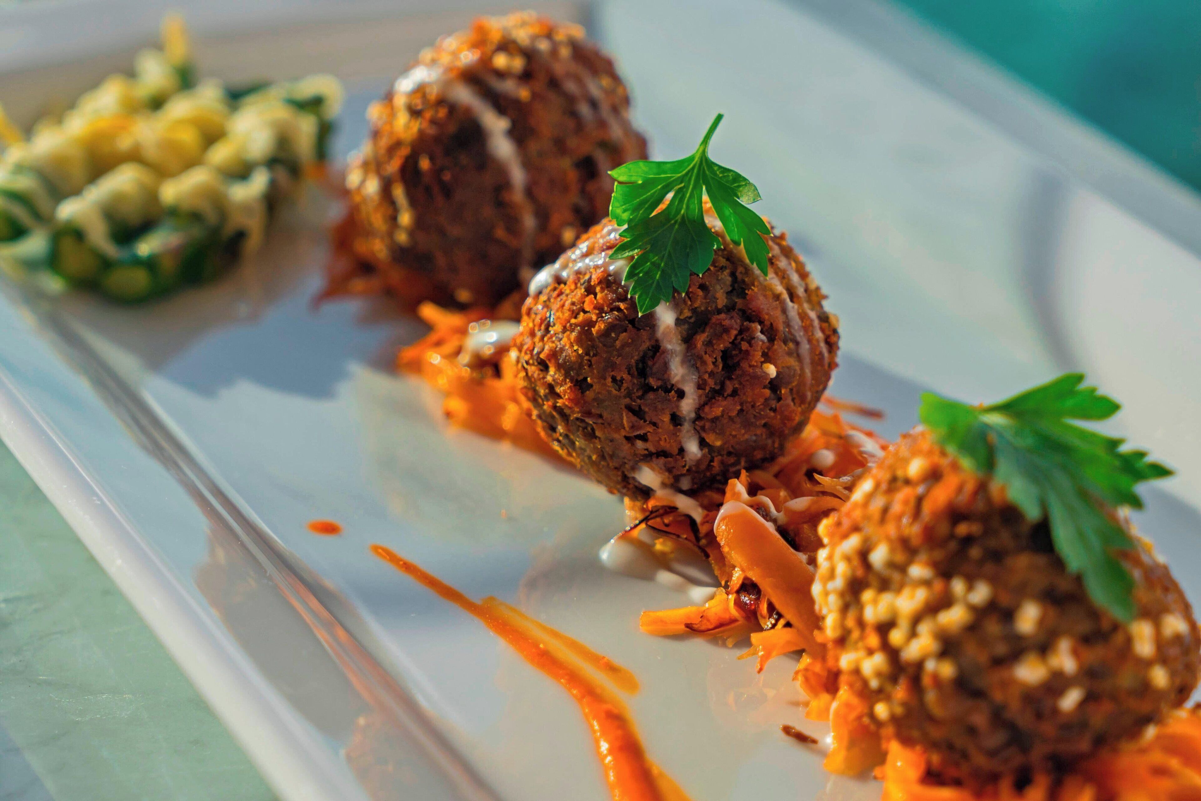 Un plat composé de trois boulettes de viande, garni de persil, accompagné d’une portion de maïs et d’une sauce.