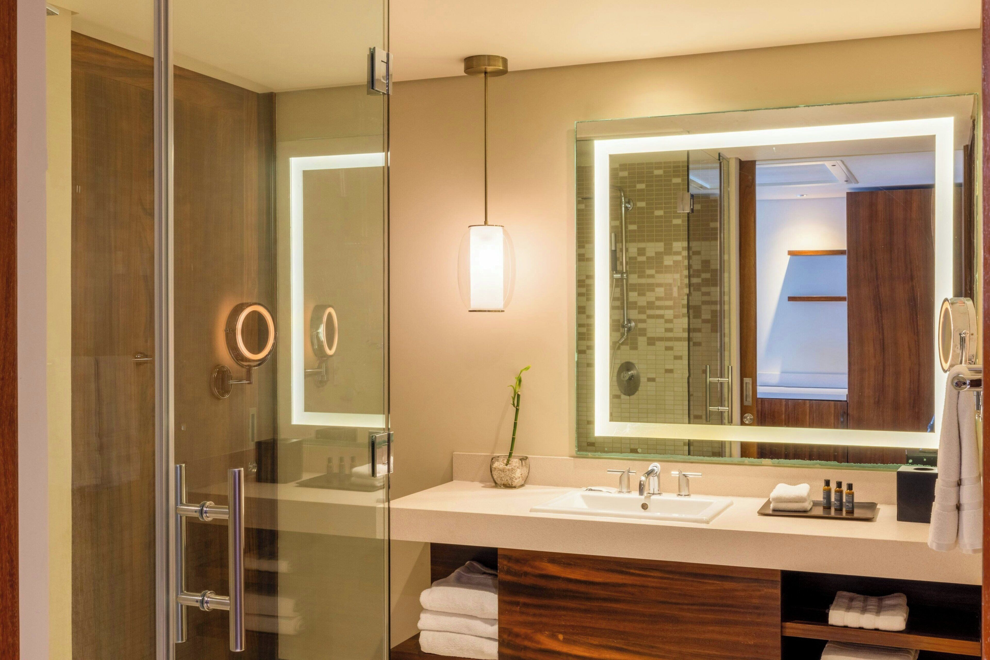 Une salle de bain moderne dotée d’une cabine de douche en verre, d’un grand miroir et d’un meuble-lavabo avec un évier et un porte-serviettes.