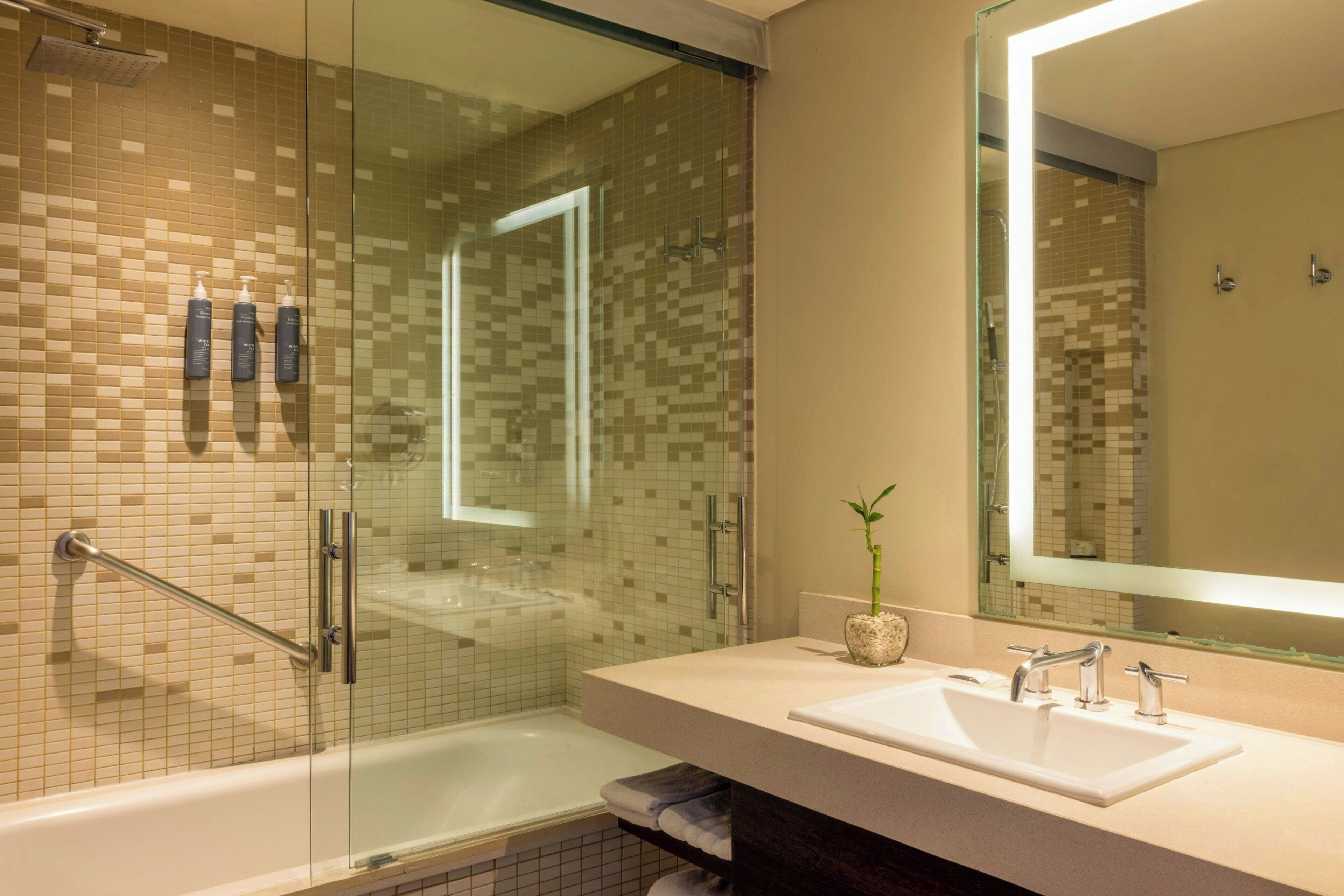 A modern bathroom with a glass-enclosed shower, a white sink, and a large mirror.