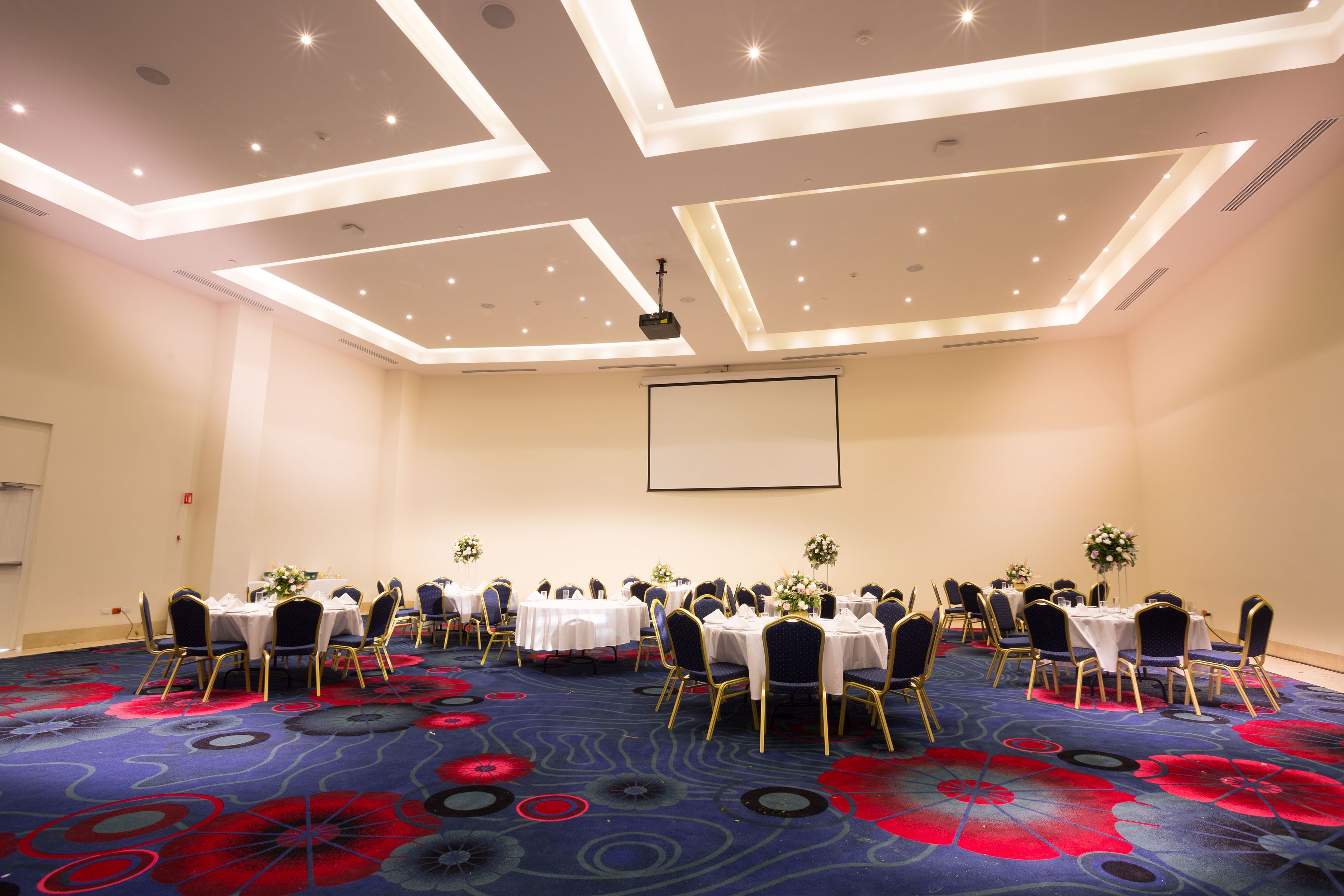 A conference room with round tables, chairs, and a projector screen.
