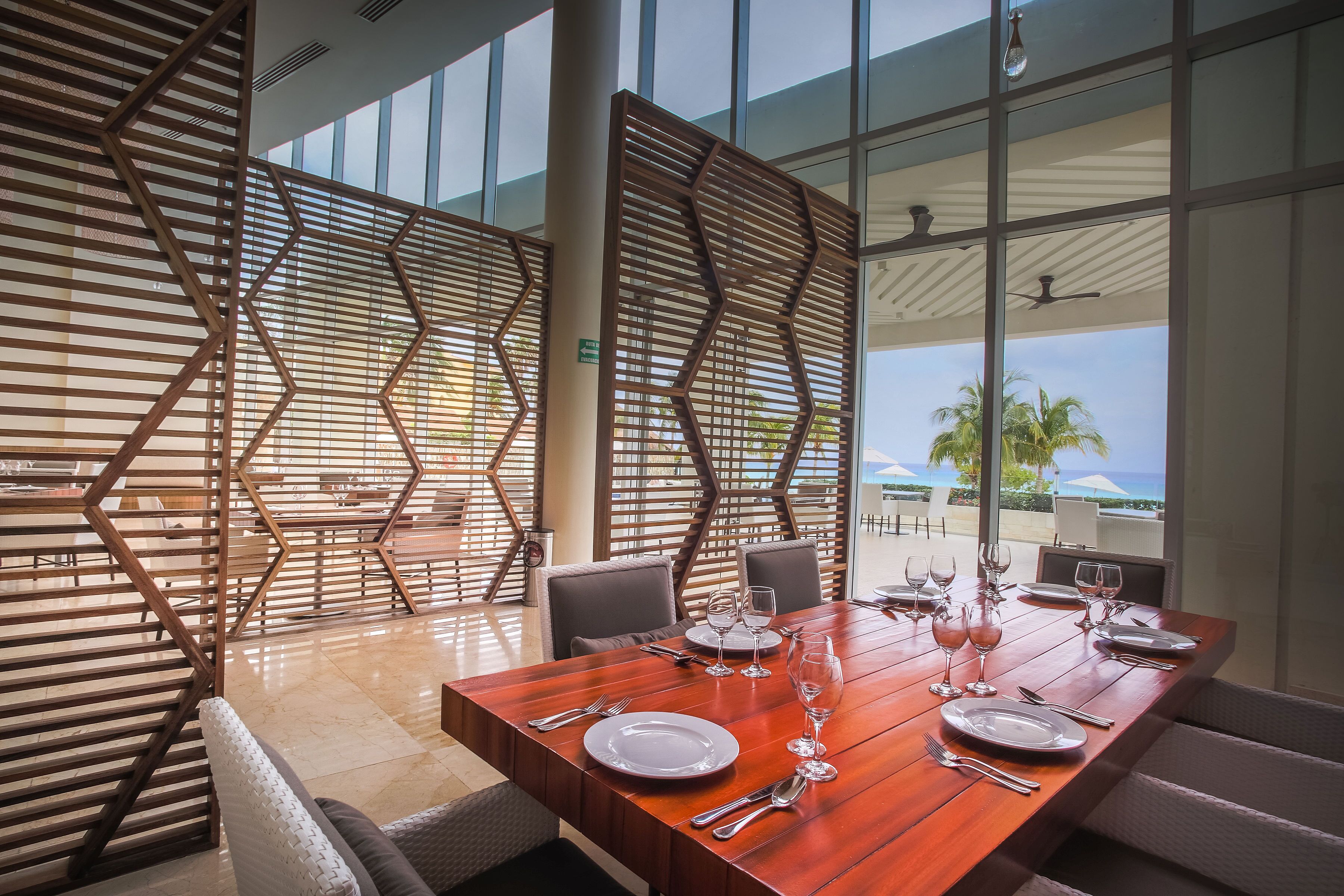 A dining area with a wooden table set for four, large windows, and a view of the outdoors.