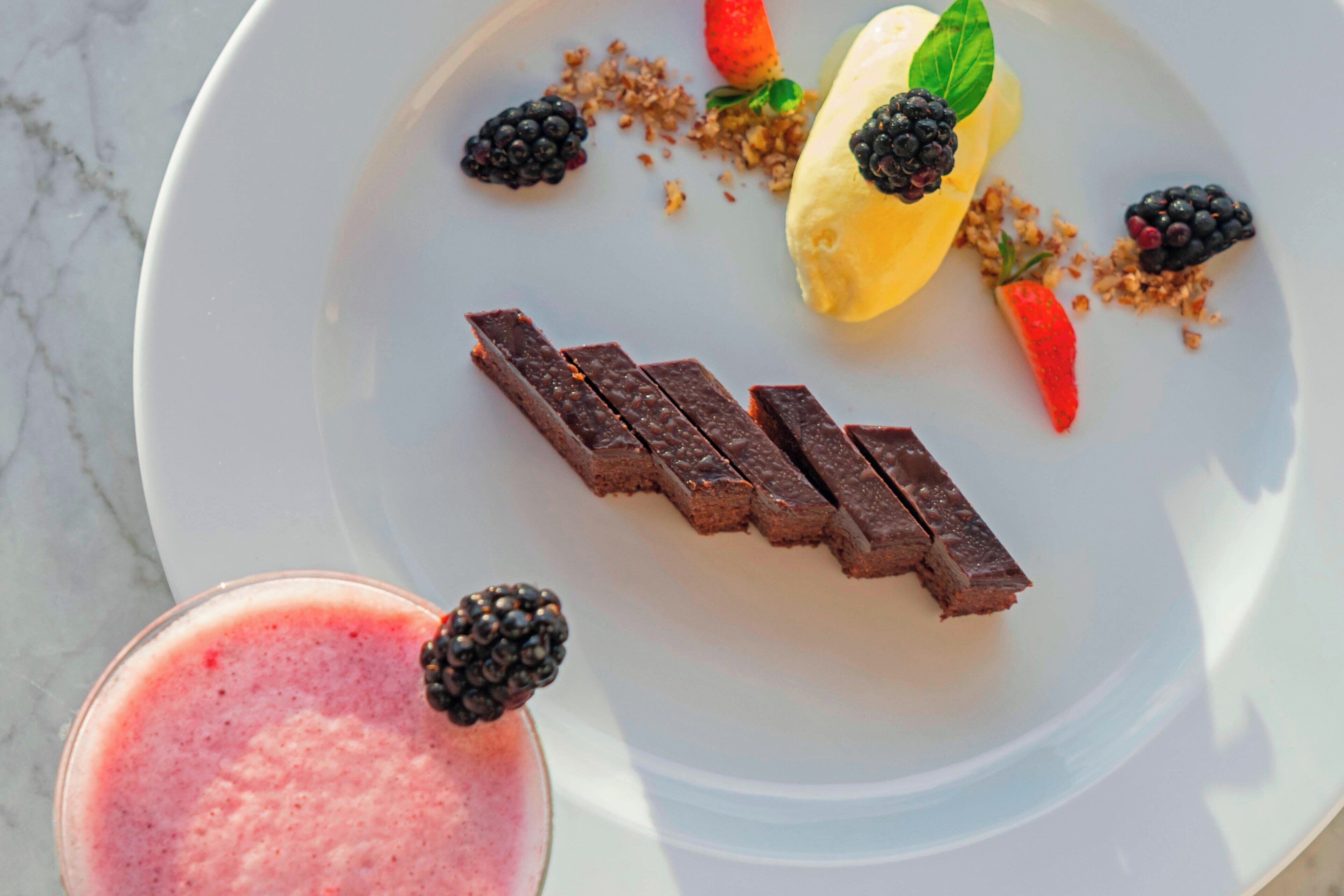 A dessert plate with chocolate pieces, a banana, berries, and a berry smoothie.