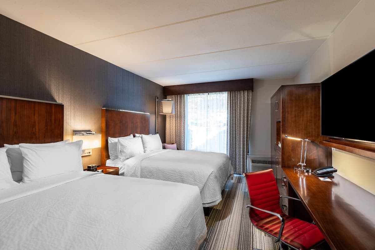 Une chambre d’hôtel avec deux lits, un bureau avec une chaise, une télévision et une fenêtre avec des rideaux.