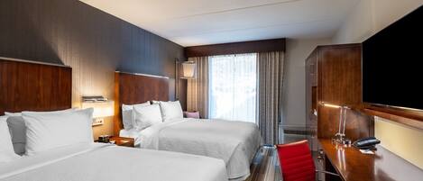 A hotel room with two beds, a desk with a chair, a TV, and a window with curtains.