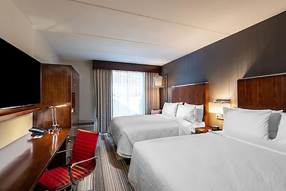 A hotel room with two beds, a desk, a TV, and a red chair.