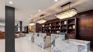 Een lobby met marmeren receptiebalies, donker houten kasten met decoratieve objecten en moderne kroonluchters.
