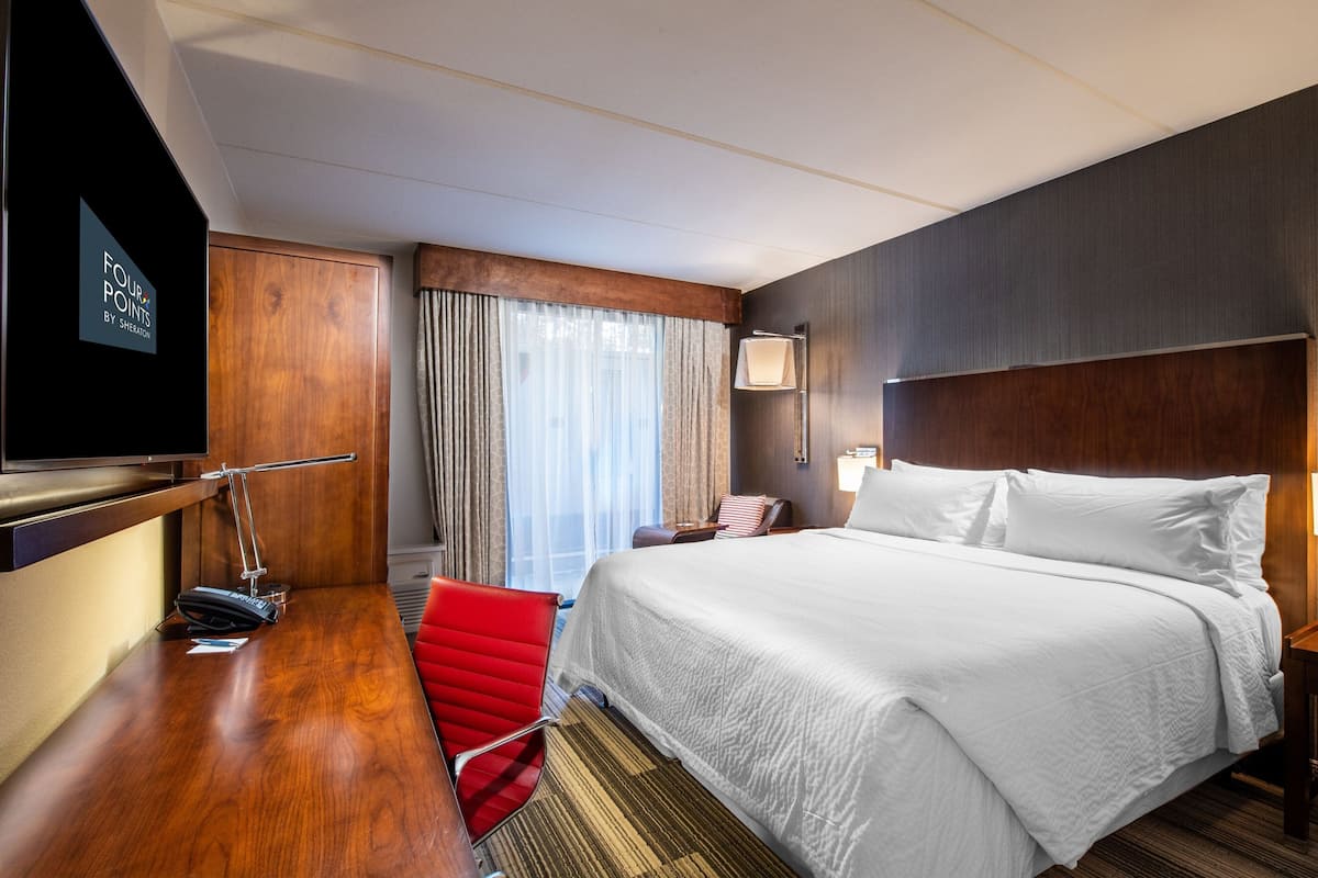 Une chambre d’hôtel avec un grand lit, un bureau avec une chaise, une télévision et une fenêtre avec des rideaux.