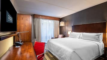 A hotel room with a large bed, a desk with a chair, a television, and a window with curtains.