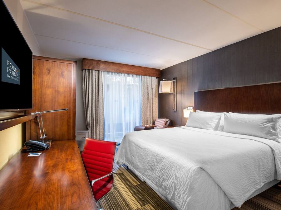 A hotel room with a large bed, a desk with a chair, a television, and a window with curtains.