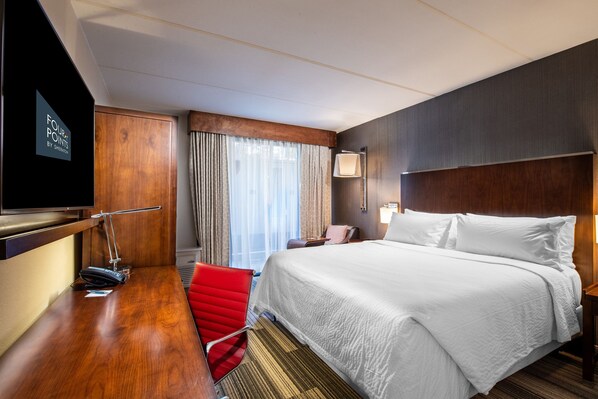 Una habitación de hotel con una cama grande, un escritorio con silla, televisión y ventana con cortinas.
