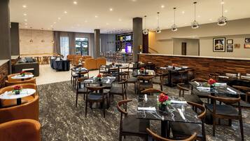 Een moderne hotel lobby met een bar, zithoeken en een trap.