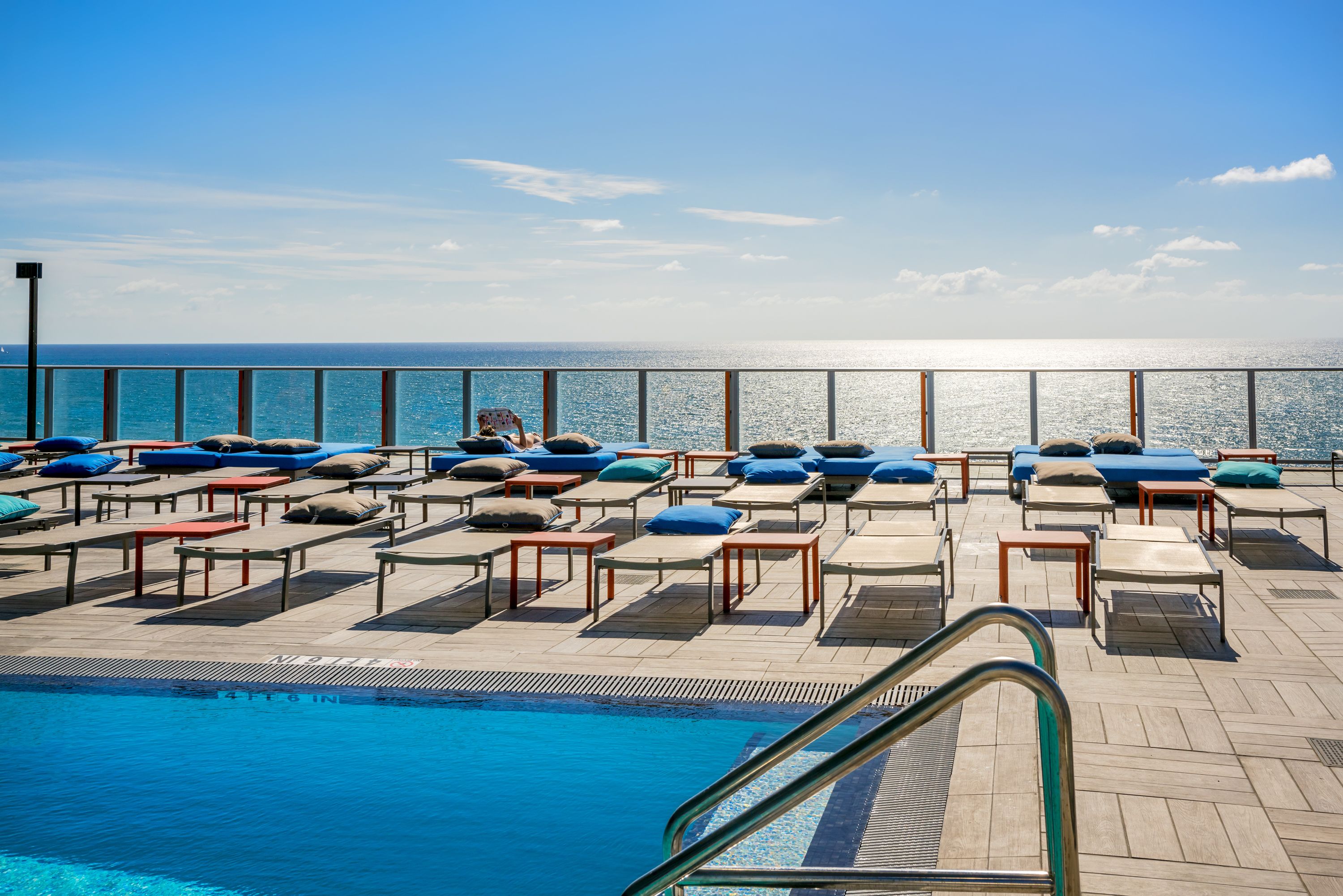 A poolside area with lounge chairs and tables, a clear view of the ocean, and a pool with a metal ladder.