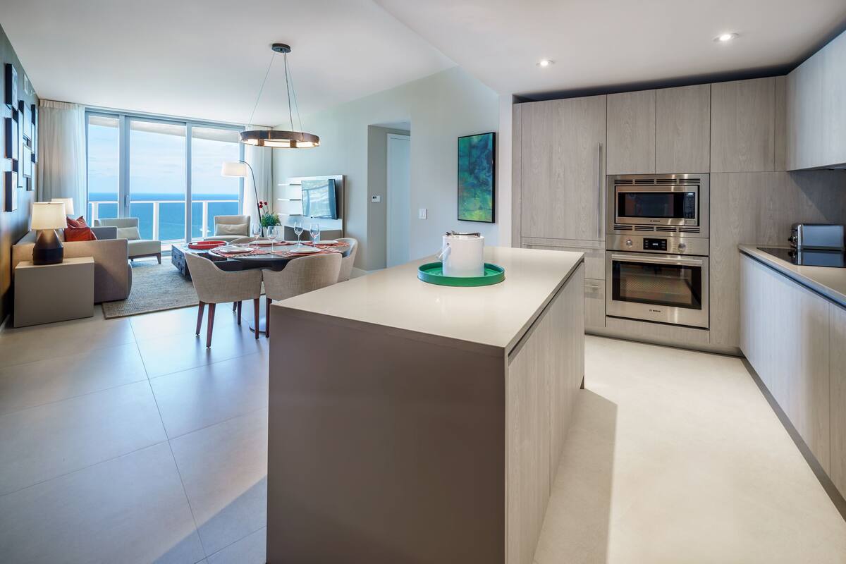 A modern kitchen with a central island, built-in appliances, and a dining area with a view of the sea.