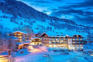 Een groot, meerhoog hotel met een skilift in de achtergrond, omringd door met sneeuw bedekte heuvels.
