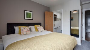 Un dormitorio con cama, mesita de noche, espejo y puerta que da al baño.