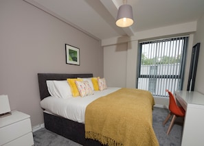Un dormitorio moderno con cama, mesita de noche y escritorio con silla.