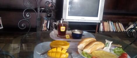 A glass table with a meal consisting of bread, vegetables, and a mango. A cup of tea and a bowl of soup are also visible.