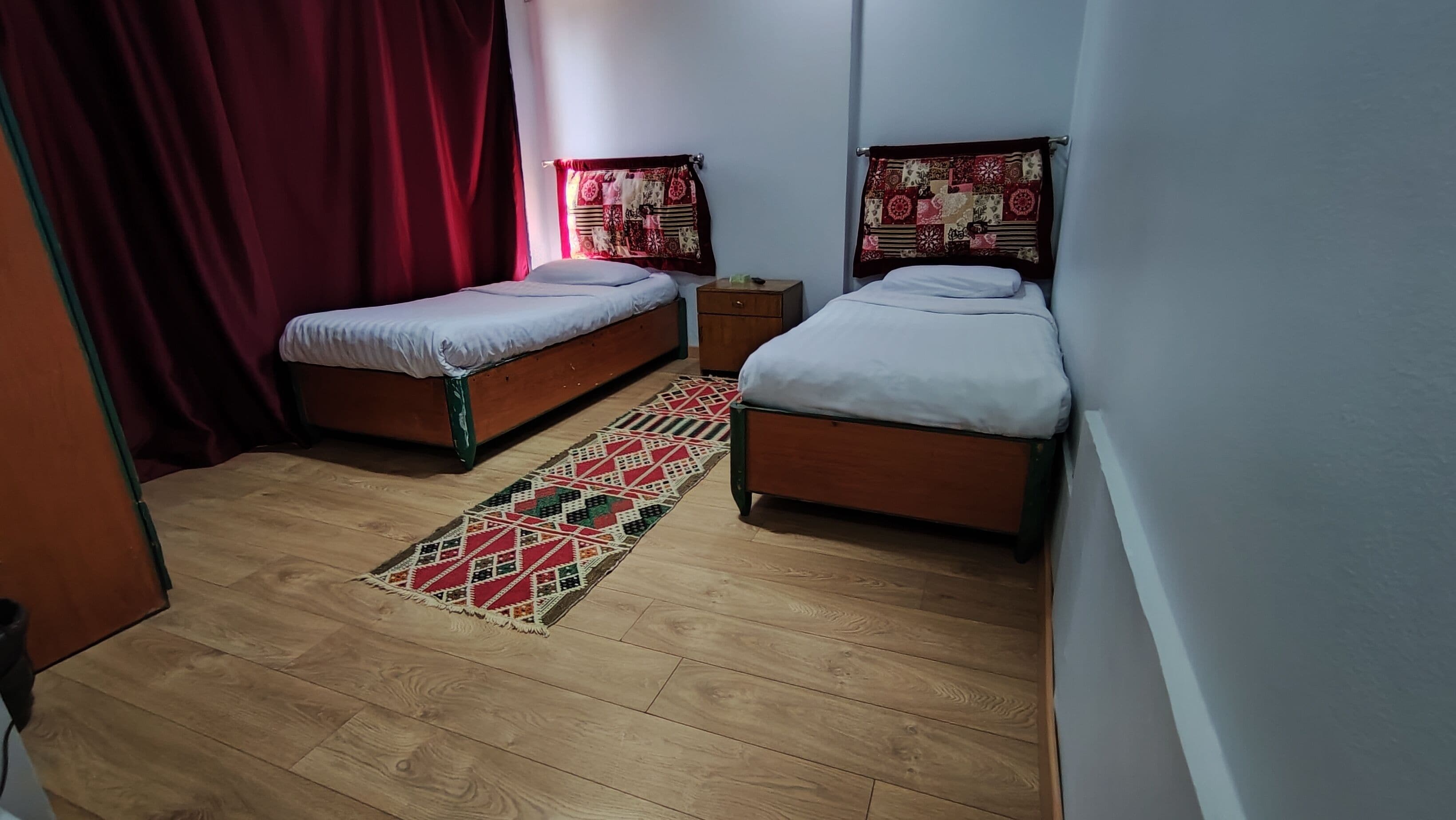 Ein kleines, gemütliches Zimmer mit zwei Einzelbetten, Holzboden und einem farbenfrohen Teppich.
