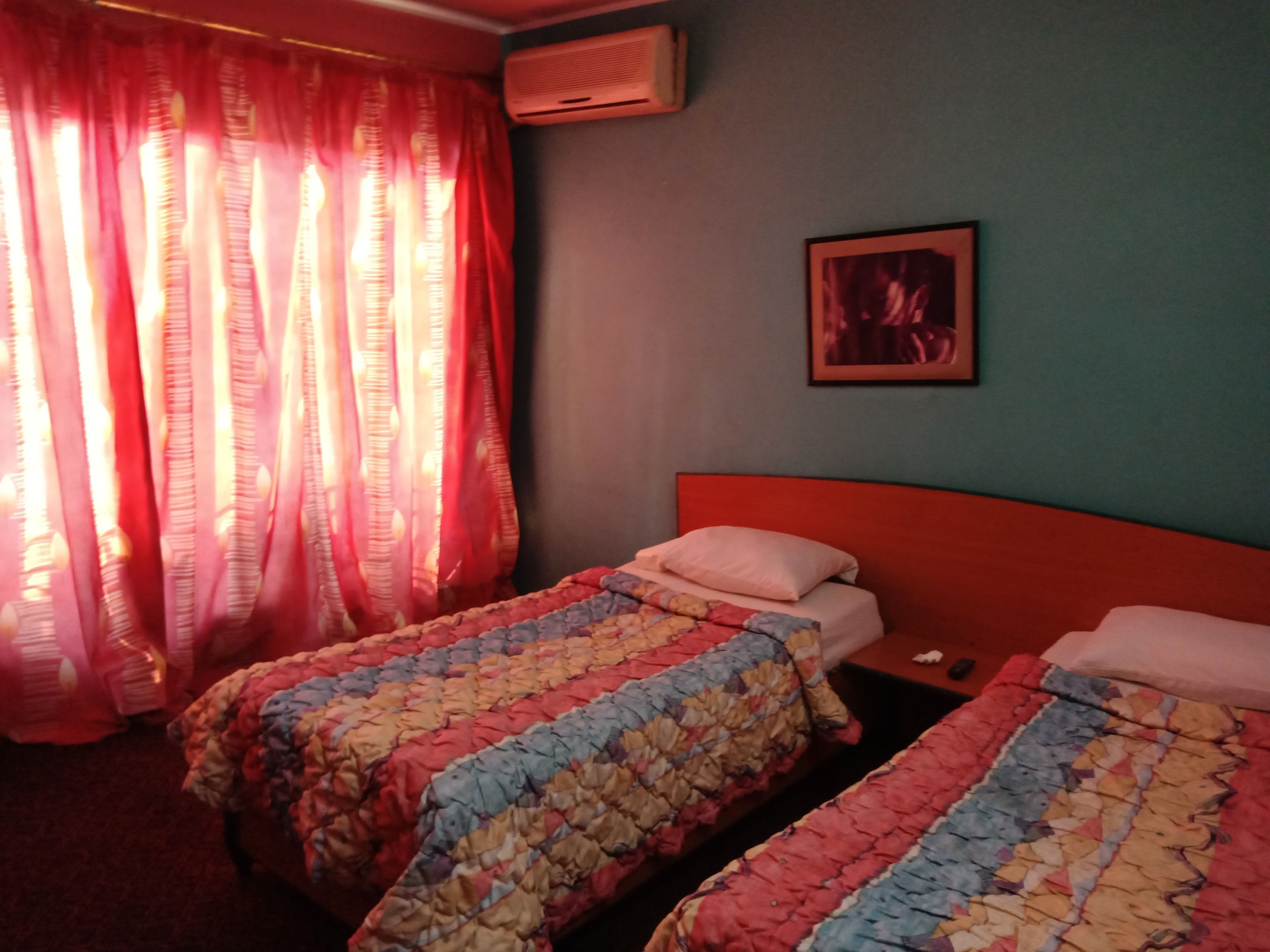A room with two beds, a red headboard, a framed picture on the wall, and an air conditioning unit.