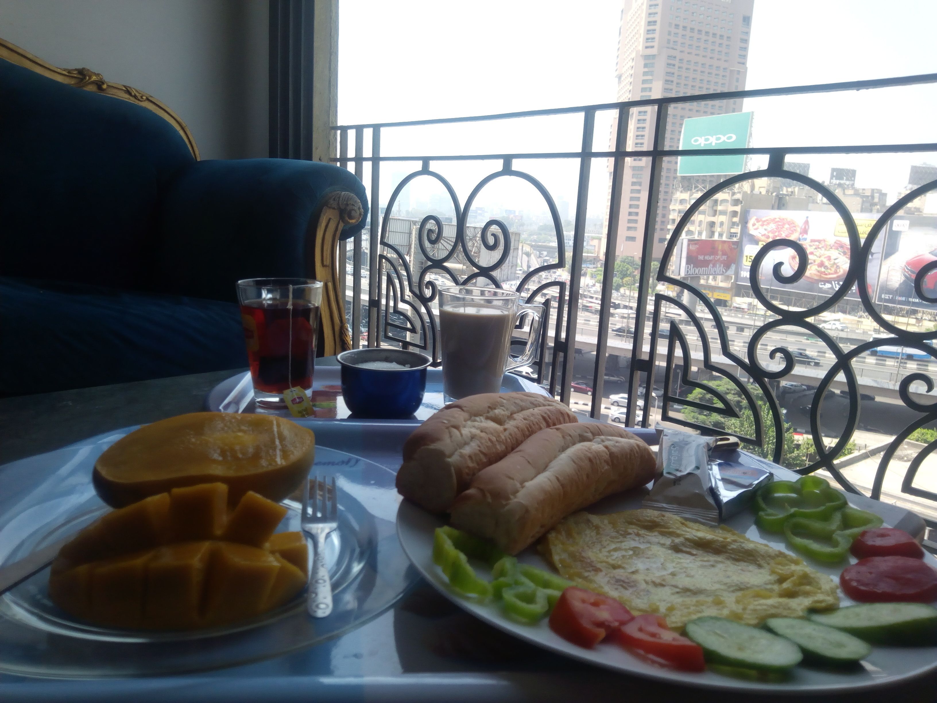 A breakfast tray with toast, eggs, and fruit on a balcony overlooking a cityscape.