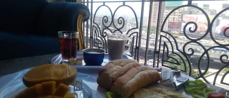 A breakfast tray with toast, eggs, and fruit on a balcony overlooking a cityscape.