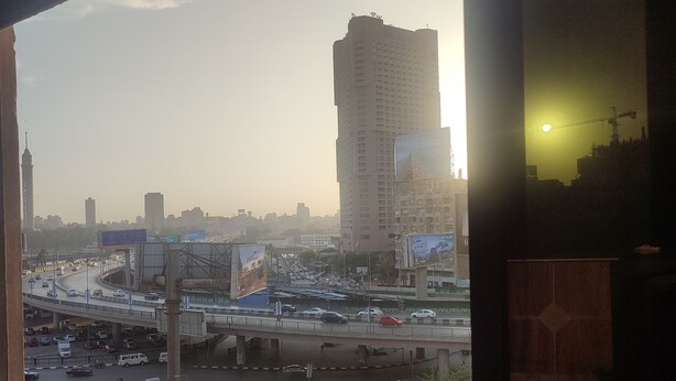 Vista desde un balcón sobre una ciudad bulliciosa, con numerosos edificios, una autopista y cielo despejado.