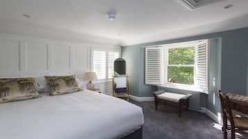 Un dormitorio con una cama grande, ropa de cama blanca, una mesita de noche con lámpara, un banco y una ventana con contraventanas.
