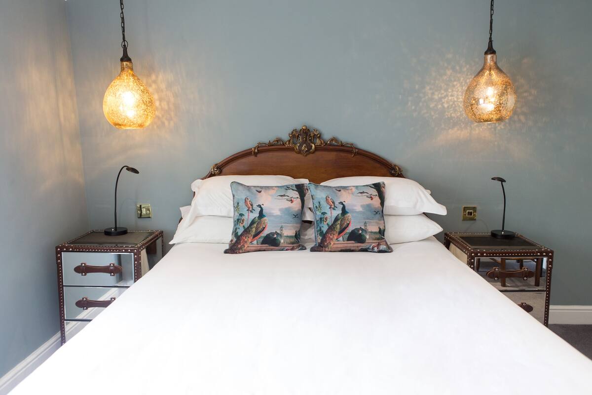 Een keurig opgemaakt bed met twee decoratieve kussens, een houten hoofdbord en twee nachtkastjes met lampen.