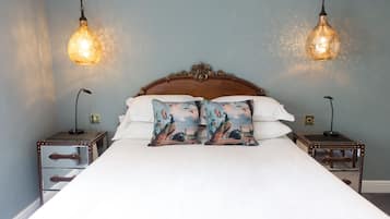 Una cama bien arreglada con dos almohadones decorativos, un cabecero de madera y dos mesitas de noche con lámparas.