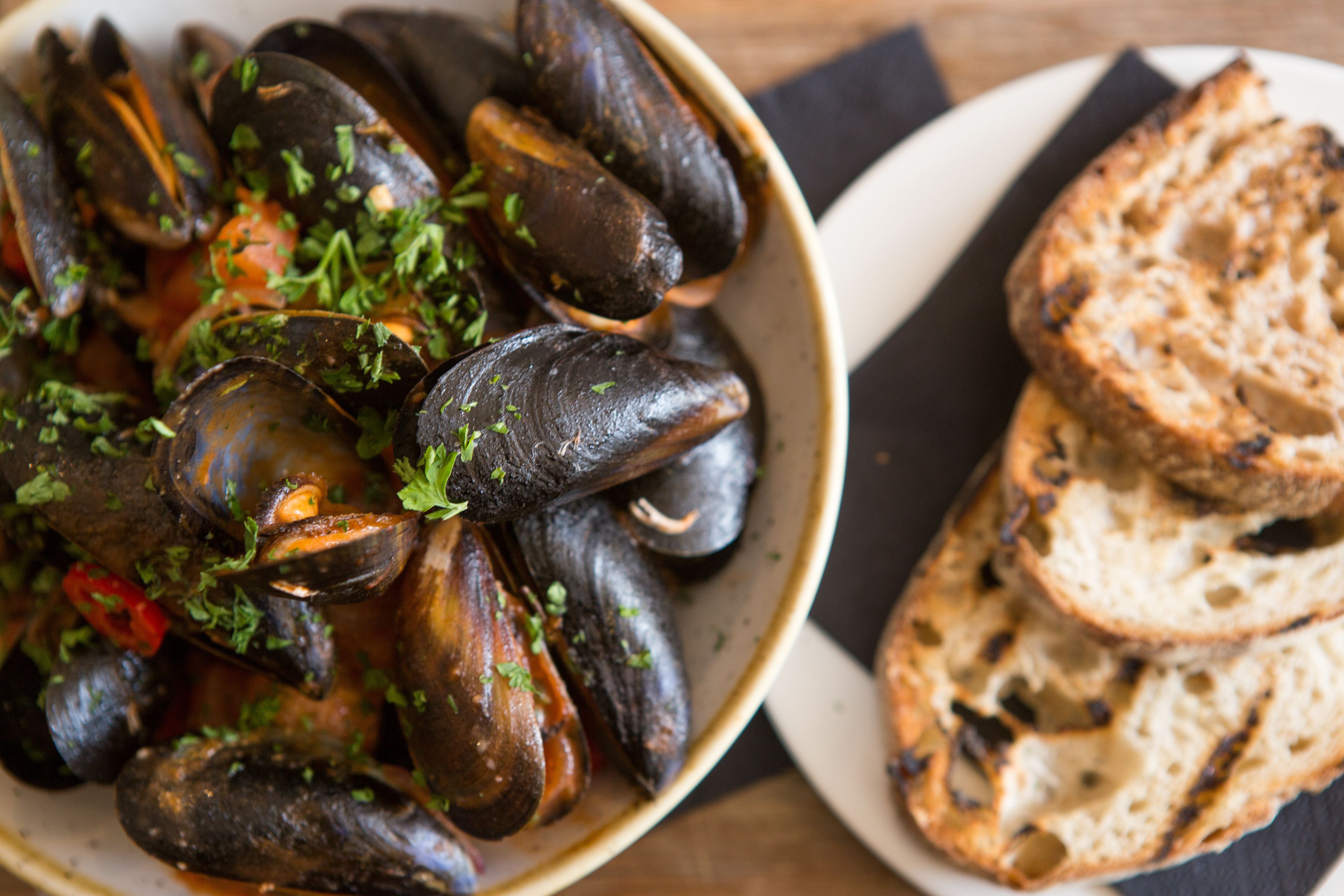 A bowl of mussels garnished with herbs, accompanied by slices of toasted bread on a plate.