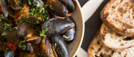 A bowl of mussels garnished with herbs, accompanied by slices of toasted bread on a plate.