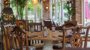 Un espace repas avec des tables et des chaises en bois, de la verrerie et une grande plante en pot.