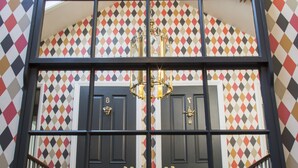 Une fenêtre donnant sur un mur orné d’un motif géométrique, un lustre et une paire de portes doubles.